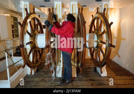 Student conservator Andrew Braund from West Dean College, cleans the helm of the Victorian battleship HMS Warrior at Portsmouth Historic Dockyard, as part of National Spring Cleaning Week. The conservation team have been researching and trialling a different way to treat the brass, using less abrasive techniques and a coating system that works well with the environment. Launched in 1860, HMS Warrior was Britain's first iron-hulled warship and had a lasting influence on naval architecture and design. Picture date: Tuesday March 22, 2022. Stock Photo