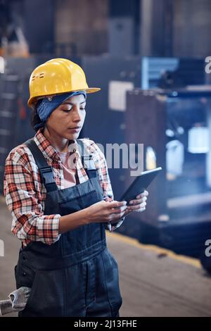 Serious female worker of industrial plant using tablet for check-up of online orders while standing in distribution warehouse Stock Photo