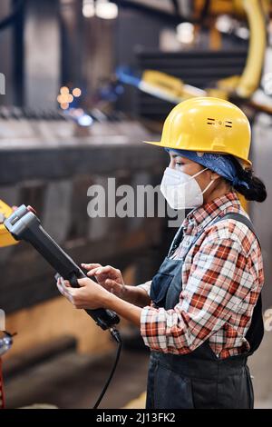 Side view of contemporary technician of factory using switch device to control work of industrial machine in warehouse Stock Photo