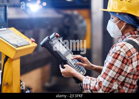 Female worker of plant in respirator and hardhat touching screen of switch device to control work of industrial machines Stock Photo