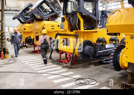 Blurry figures of two contemporary engineers of factory in workwear moving along row of industrial machines Stock Photo