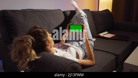 Woman staying home and waching horizontal phone Green Mock-up Screen Chroma key. Stock Photo