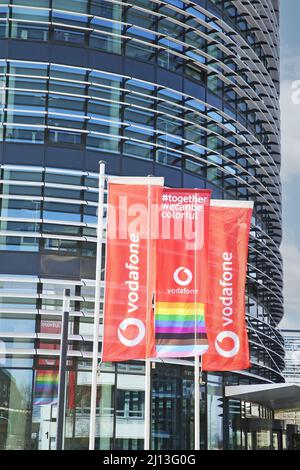 Düsseldorf (Vodafone campus) - March 9. 2022: View on red flags at modern futuristic administration building entrance against blue sky Stock Photo