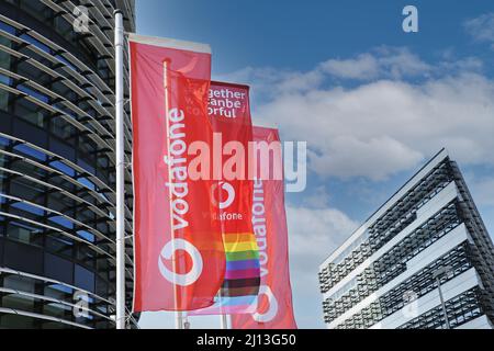 Düsseldorf (Vodafone campus) - March 9. 2022: View on red flags at modern futuristic administration building entrance against blue sky Stock Photo