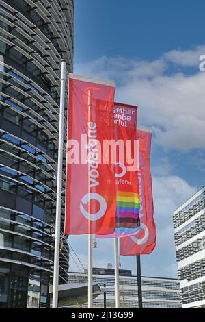 Düsseldorf (Vodafone campus) - March 9. 2022: View on red flags at modern futuristic administration building entrance against blue sky Stock Photo