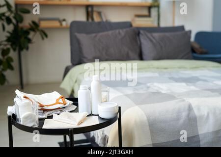 Group of bodycare items for baby on small round table against double bed with cushions and duvet in spacious bedroom Stock Photo