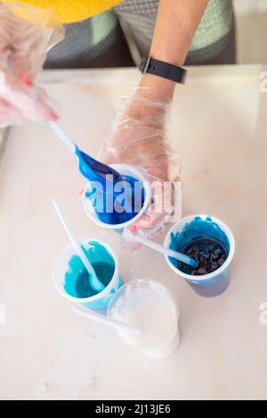 Epoxy resin different blue color in cup for casting stabilizing wood, abstract art. Process of making accessory from resin.Mixing colorful of resin Stock Photo