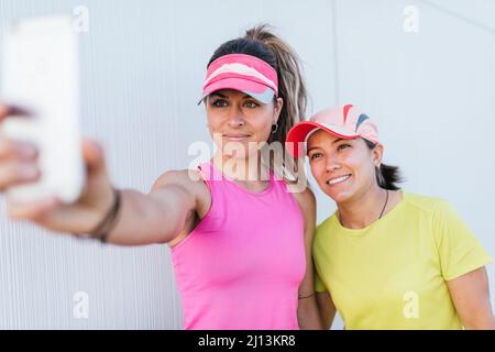 Two fit woman wearing sportswear taking selfie photo while working out in city. Two sports women smiling and doing selfie after running. Stock Photo
