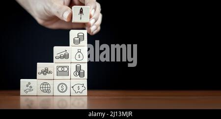 Hand placed wooden cube block of money saving icon. Banknote. Stacked wooden blocks with money bag sign. The process of growing a successful business Stock Photo