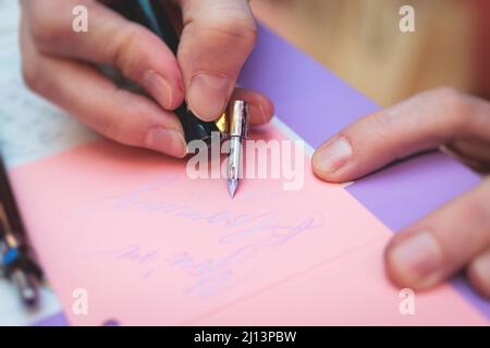 Process of calligraphy handwriting with an ink fountain pen feather, calligrapher practicing writing on postcard paper using pen brush and sign pen wi Stock Photo