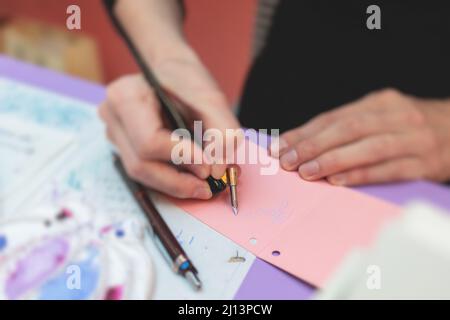 Process of calligraphy handwriting with an ink fountain pen feather, calligrapher practicing writing on postcard paper using pen brush and sign pen wi Stock Photo
