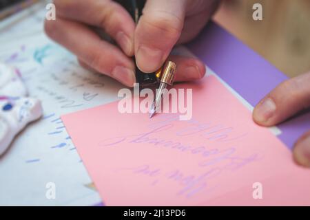 Process of calligraphy handwriting with an ink fountain pen feather, calligrapher practicing writing on postcard paper using pen brush and sign pen wi Stock Photo