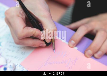 Process of calligraphy handwriting with an ink fountain pen feather, calligrapher practicing writing on postcard paper using pen brush and sign pen wi Stock Photo