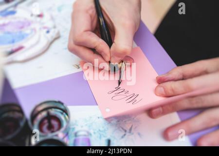 Process of calligraphy handwriting with an ink fountain pen feather, calligrapher practicing writing on postcard paper using pen brush and sign pen wi Stock Photo