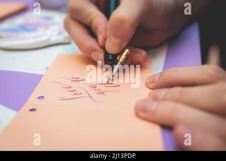 Process of calligraphy handwriting with an ink fountain pen feather, calligrapher practicing writing on postcard paper using pen brush and sign pen wi Stock Photo