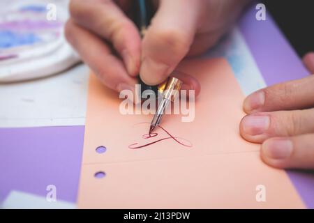 Process of calligraphy handwriting with an ink fountain pen feather, calligrapher practicing writing on postcard paper using pen brush and sign pen wi Stock Photo