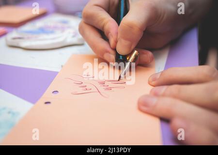 Process of calligraphy handwriting with an ink fountain pen feather, calligrapher practicing writing on postcard paper using pen brush and sign pen wi Stock Photo