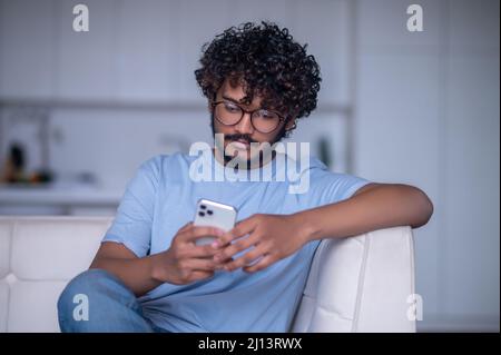 Focused Indian guy reading a text message on his gadget Stock Photo