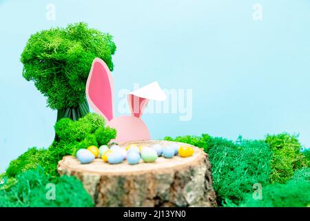 The pink rabbit hides behind a stump. Easter greeting card with Easter symbols. Stock Photo