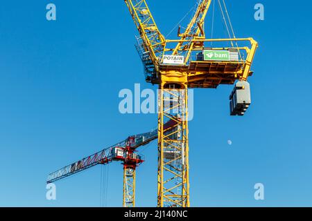 Two mechanical cranes towering above an urban construction site, the rising moon in a blue sky, London, UK Stock Photo