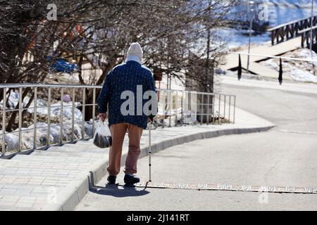 Old woman with cane walks in spring park. Healthy lifestyle in old age, life in retirement Stock Photo