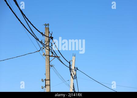 Power line posts with tangled electrical wires and capacitors on blue sky background. Electricity transmission line, power supply Stock Photo