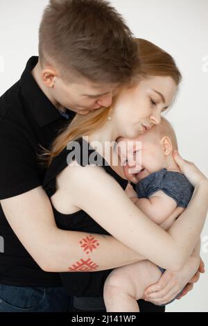 Vertical mom and dad, family caring and holding wailing depressed baby in arms. Temperature because of tooth ache, pain Stock Photo