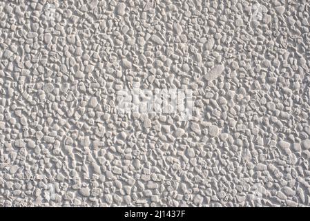 a wall covered with small pebbles and painted white in bright sunshine Stock Photo