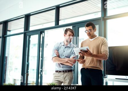 Progressing on their team project. Shot of two young designers working on a digital tablet in an office. Stock Photo