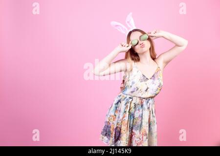 Girl in a dress with rabbit ears on a pink background, Easter holidays. Woman beautiful with long hair, easter eggs closes her eyes Stock Photo