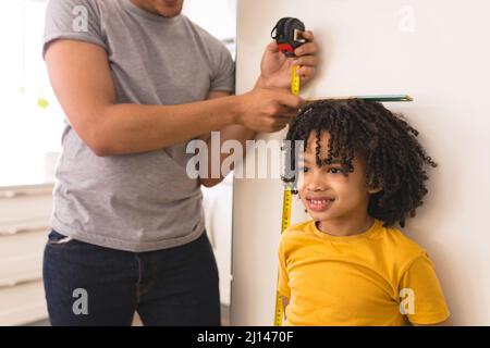 Hispanic man measuring son's height with tape and ruler against white wall at home Stock Photo