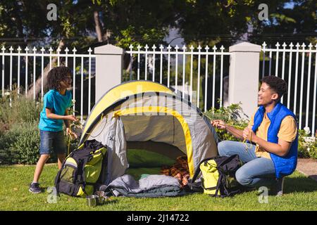 Happy hispanic father and son pitching tent together for camping at backyard on sunny day Stock Photo