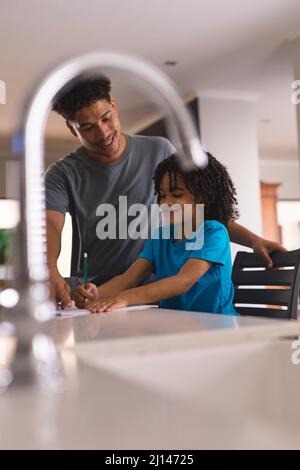 Smiling hispanic man assisting son with homework in kitchen at home Stock Photo