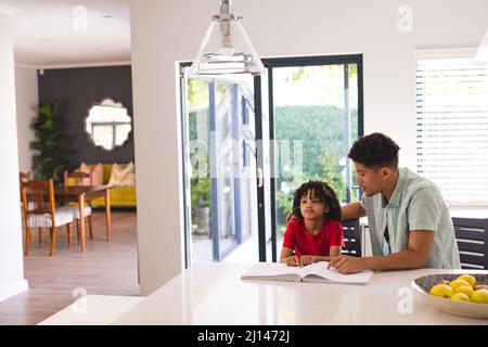 Hispanic father sitting beside blind son reading book with braille in kitchen at home Stock Photo