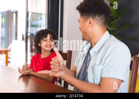 Happy hispanic father teaching sign language to mute son while sitting at dining table Stock Photo