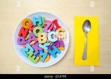 Large white porcelain soup bowl full of wood block letters in bright colors with A, B and C on top of alphabet. Bright yellow napkin with spoon to sid Stock Photo