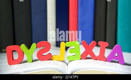 Bright colorful wooden toy blocks on an open book spelling dyslexia. Learning challenges disabilities. S, L and E are backwards. Hard bound books line Stock Photo
