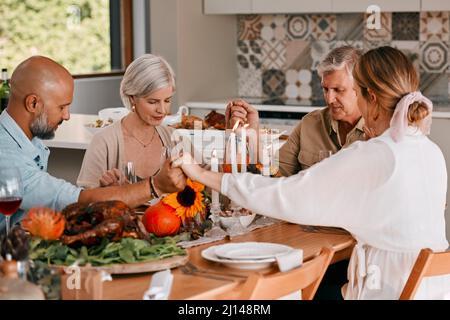 May we be grateful for good friends everyday. Shot of a group of mature friends joining hands in prayer before having a Thanksgiving meal. Stock Photo