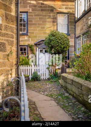 Traditional stone built cottage with white picket fence, situated in a narrow back alley in the old town of Robin Hoods Bay, North Yorkshire. Stock Photo