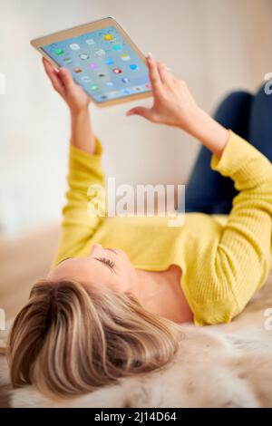 So many apps to keep her company. A rear view shot of a young woman using a digital tablet at home. Stock Photo