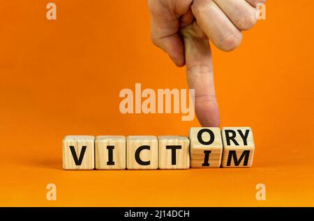 From victim to victory symbol. Businessman turns wooden cubes and changes concept words Victim to Victory. Beautiful orange background. Business suppo Stock Photo