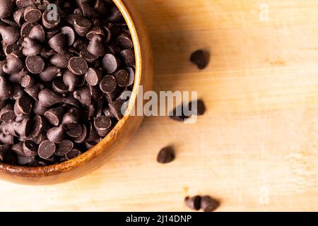 Overhead view of chocolate chips in bowl on wooden cutting board Stock Photo