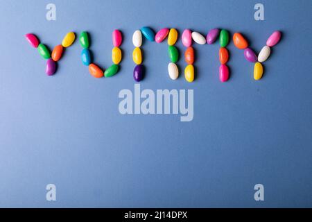 Overhead view of yummy word arranged from multi colored candies on blue background over copy space Stock Photo