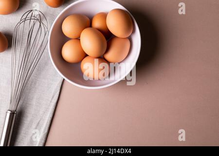 Overhead view of fresh brown eggs in bowl by wire whisk on table with copy space Stock Photo