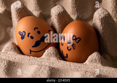 Close-up of creative male and female drawing on brown eggs in carton Stock Photo
