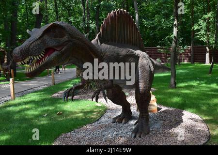 DINO PARK, KHARKOV - AUGUST 8, 2021: Day view of beautiful Dinosaur sculpture display in the park. Spinosaurus stands in a forest. Spinosaurus was a r Stock Photo