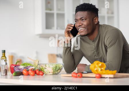 Mobile communication. Happy handsome black man talking on cellphone in kitchen Stock Photo