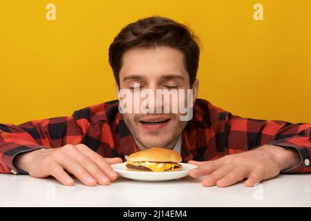 Closeup Of Excited Guy Smelling Tasty Burger At Studio Stock Photo