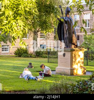 The statue of Bishop Henry Wardlaw watching over two female students studying in St Marys College Quadrangle, University of St Andrews, Fife, Scotland Stock Photo