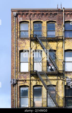 Seattle - March 20, 2022; Yellow paint peeling on an old  red brick building with a black metal  fire escape and rows of windows Stock Photo